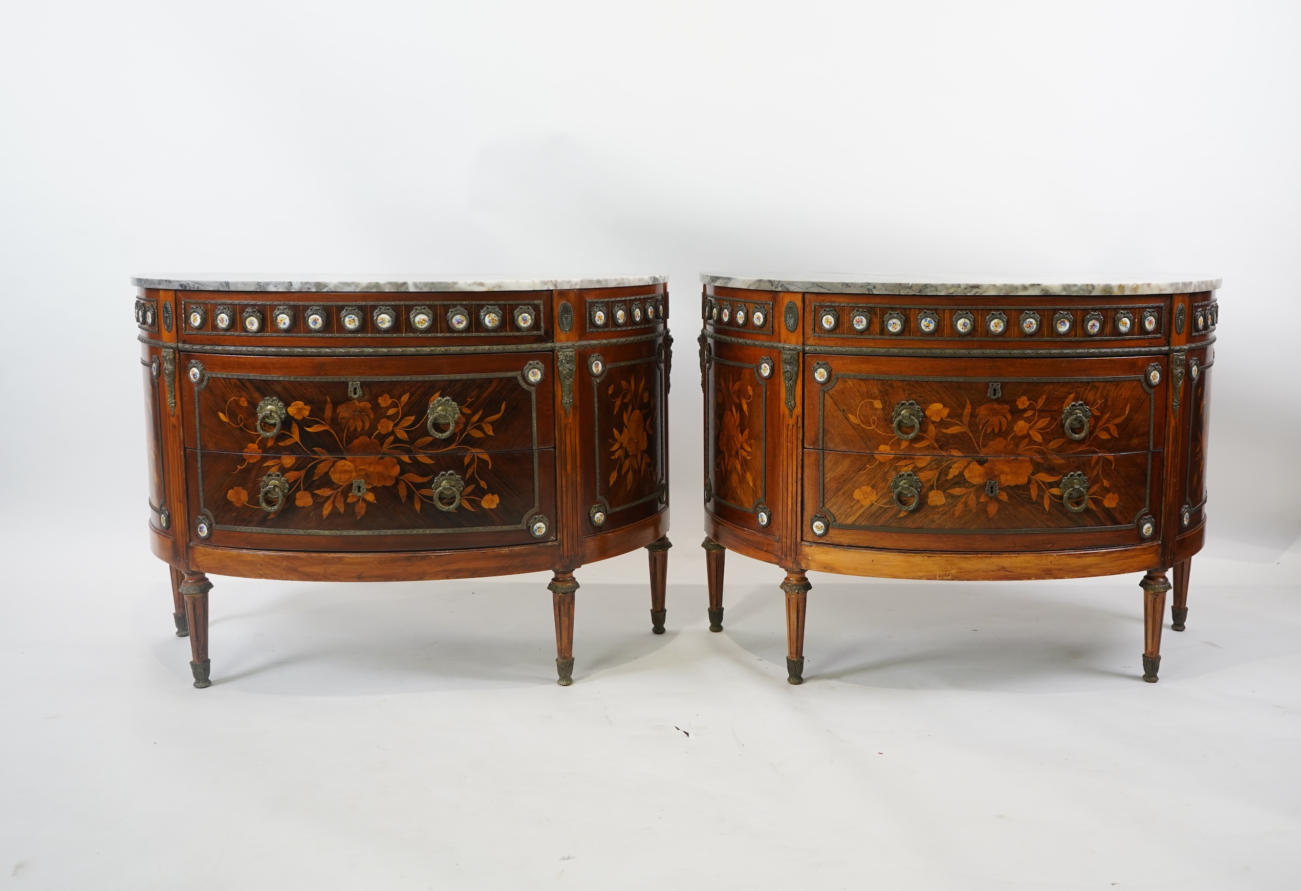 A pair of early 20th century French marquetry inlaid, gilt metal and porcelain mounted rosewood and beech demi-lune commodes